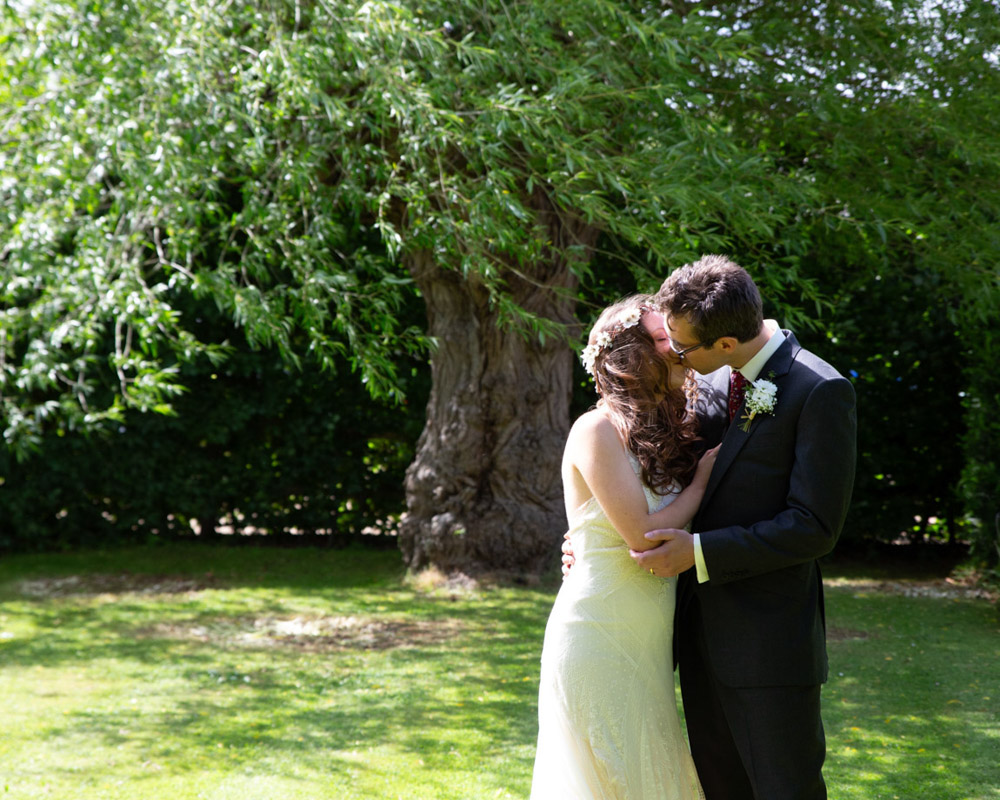 Natural summer couple portrait in Yorkshire of a couple kissing on the lawn, with soft light and a gentle breeze moving through the trees captured by a Leeds wedding photographer